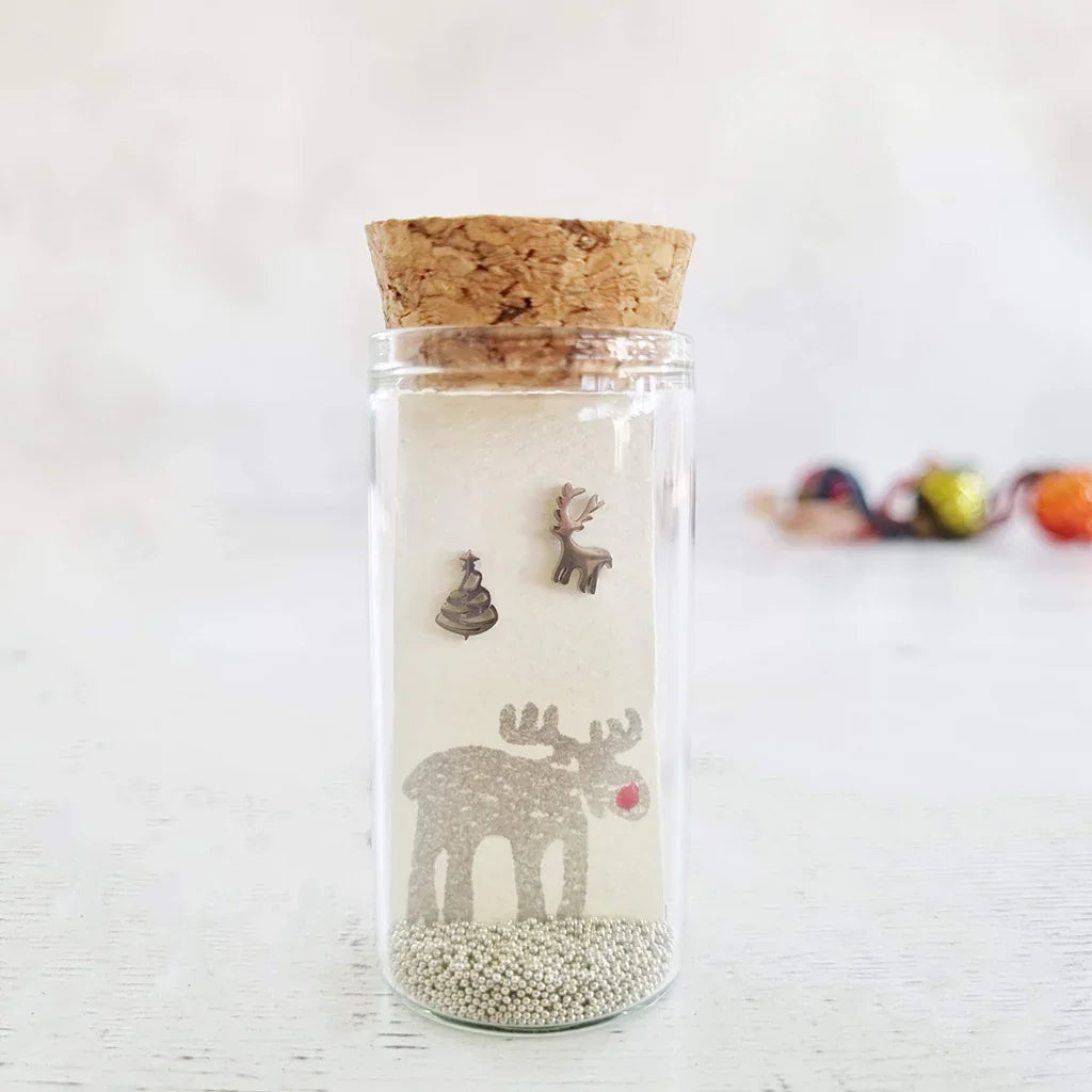 Rudolf reindeer stud earrings in a small glass bottle with a cork stopper, beside a wrapped Christmas gift